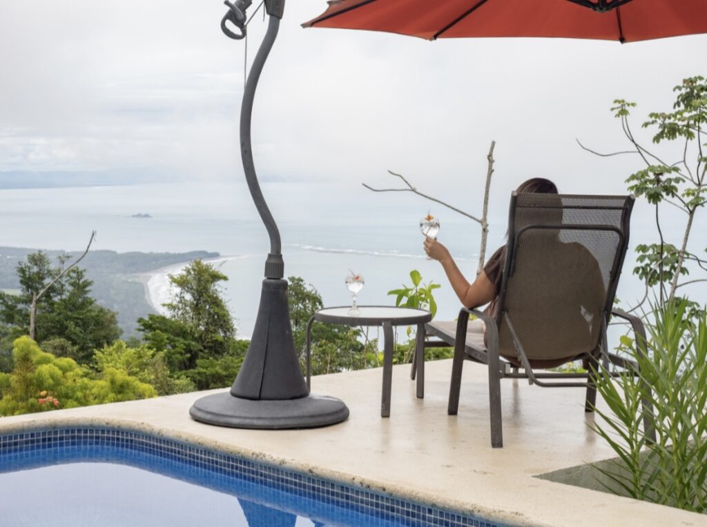 Guest relaxing with a drink on a private terrace overlooking the Pacific coastline at a boutique jungle hotel in Costa Rica, with a pool and lush tropical surroundings.